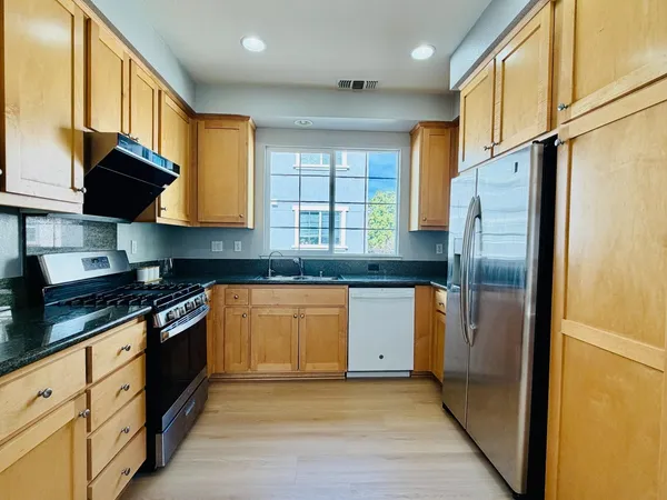 a kitchen with stainless steel appliances granite countertop a refrigerator a stove and a sink