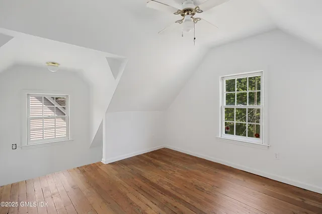 an empty room with wooden floor chandelier fan and windows