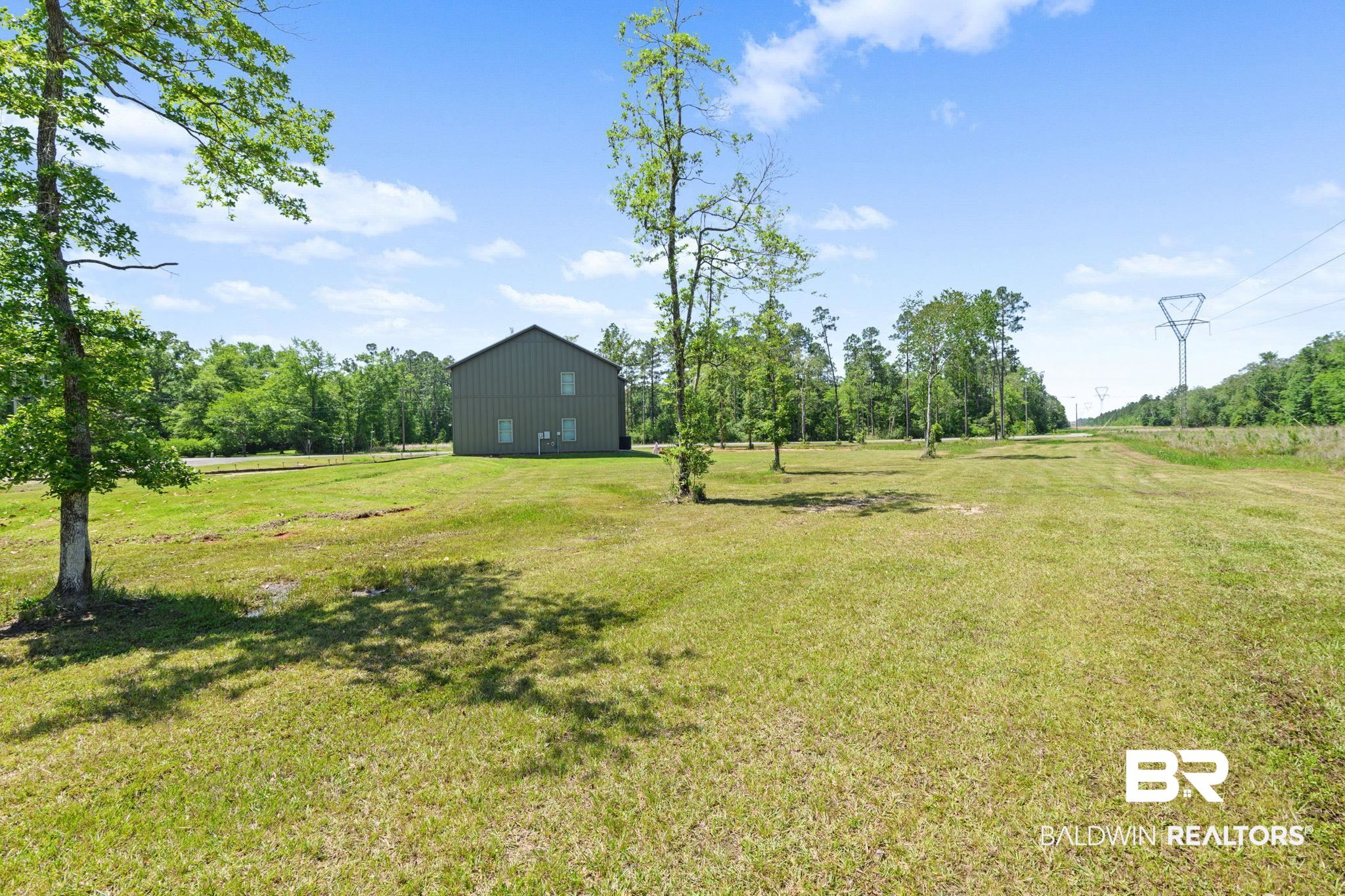 11025 Creax Road Axis, AL 36505 - Photo 8 of 45 Expansive grassy lot featuring mature trees and a modern metal-sided structure with multiple windows