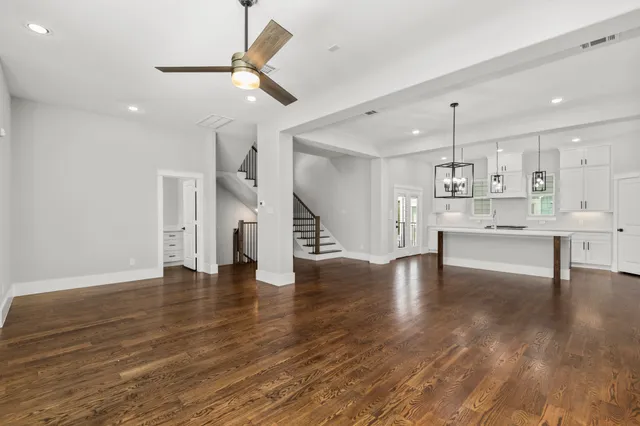 a view of an empty room with wooden floor and a ceiling fan