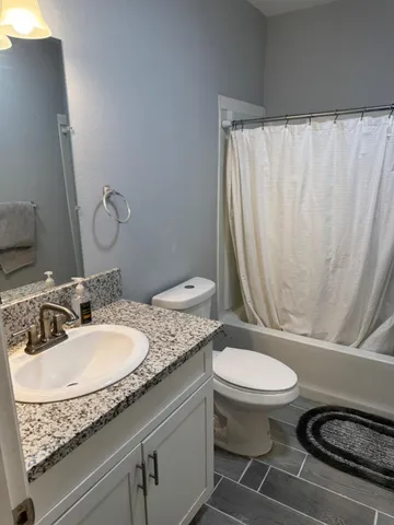 a bathroom with a granite countertop sink a toilet a mirror and shower curtain