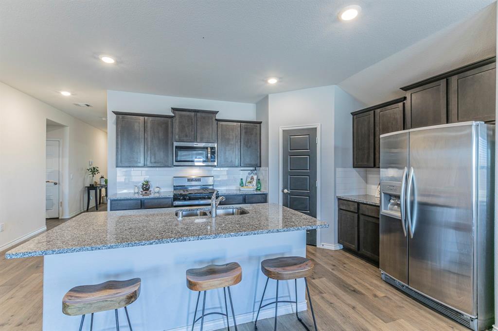 a kitchen with stainless steel appliances granite countertop a refrigerator a stove a sink a dining table and chairs