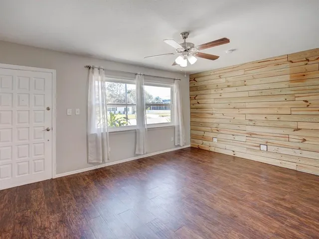 an empty room with wooden floor fan and windows