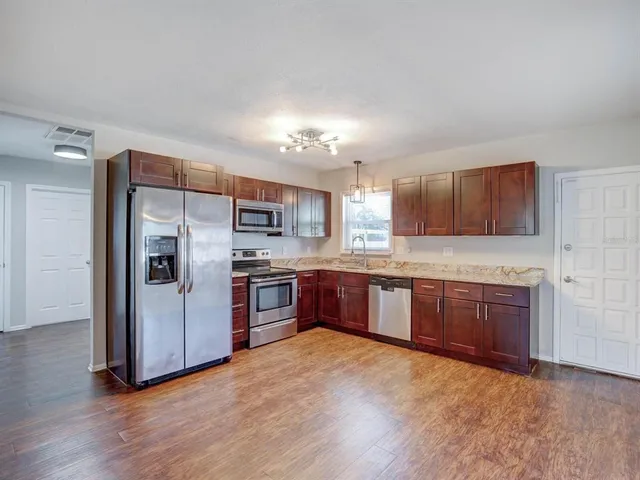 a large kitchen with stainless steel appliances granite countertop a large refrigerator a sink dishwasher a stove with wooden cabinets and floor