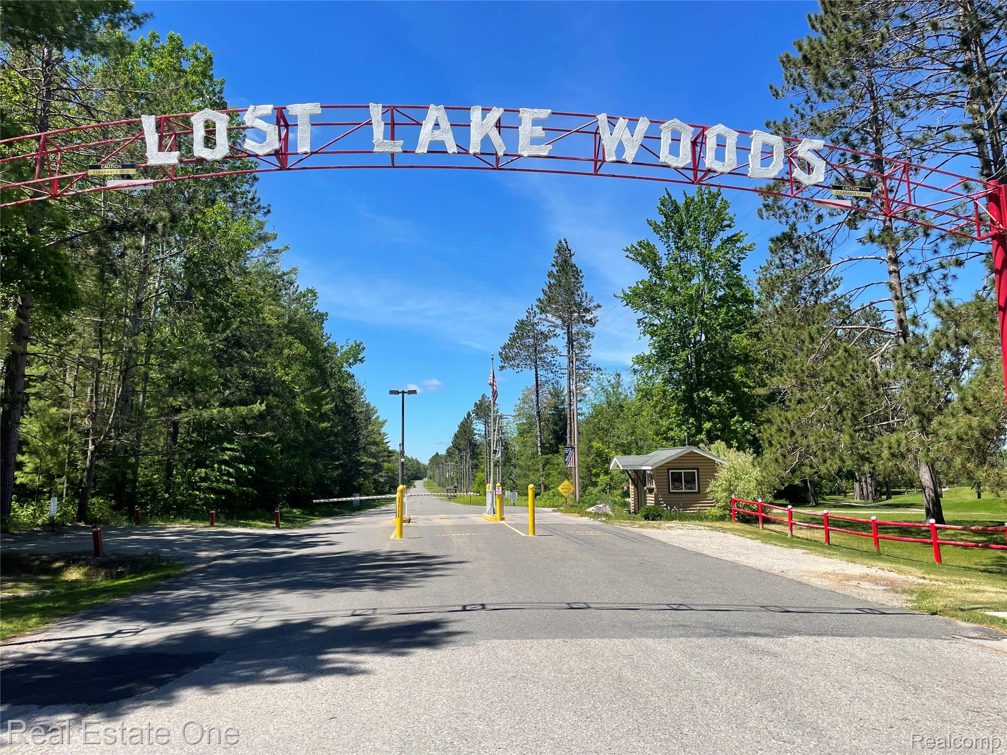 4160 Hawk Road Lincoln, MI 48742 - Photo 48 of 48 Gated community entrance featuring a prominent overhead sign, asphalt roadway, and surrounding mature trees