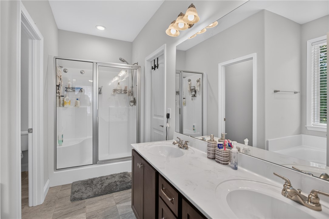 711 Barnes Road Seneca, SC 29672 - Photo 18 of 34 A well-lit primary bathroom featuring dual sinks, a spacious walk-in shower, and a large mirror.