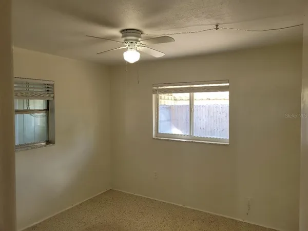 an empty room with a window and chandelier fan