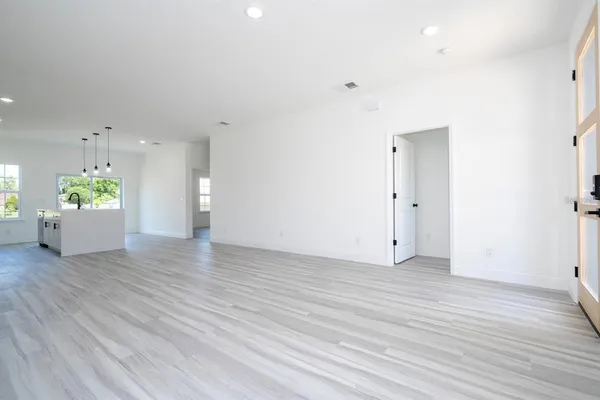 a view of an empty room with wooden floor and a kitchen