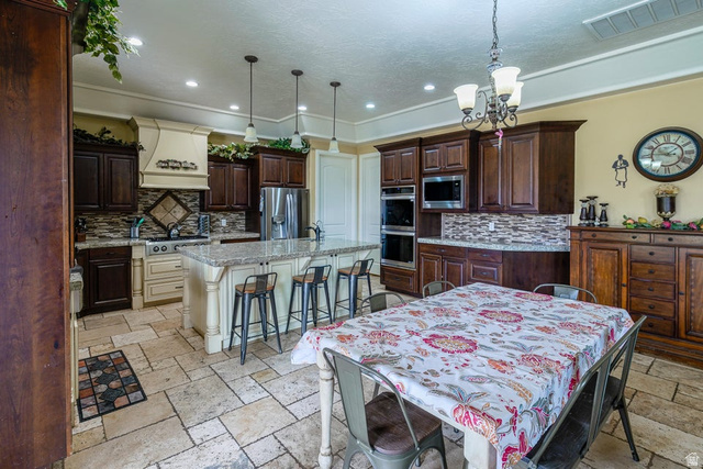 3683 South 2640 West St. George, UT 84790 - Photo 16 of 41 Kitchen featuring a center island with bar seating, dual-tone cabinetry, stone tile flooring, stainless steel appliances, and a tiled backsplash