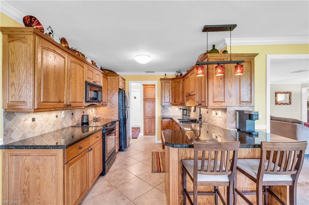 Kitchen featuring black appliances, backsplash, crown molding, a breakfast bar, and sink