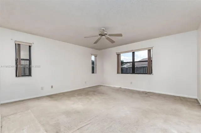 an empty room with chandelier fan and windows