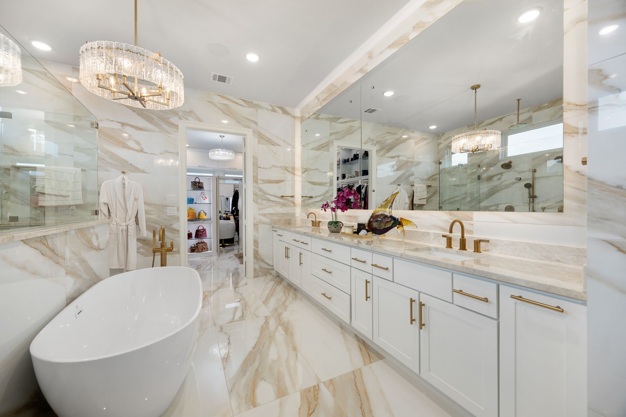 29419 Cir S Rnch Trail Fulshear, TX 77406 - Photo 18 of 45 This sophisticated primary en-suite bathroom highlights a freestanding soaking tub, a multi-cabinet white vanity with quartz countertops, custom gold-tone plumbing fixtures, and extensive marble-look tile walls.