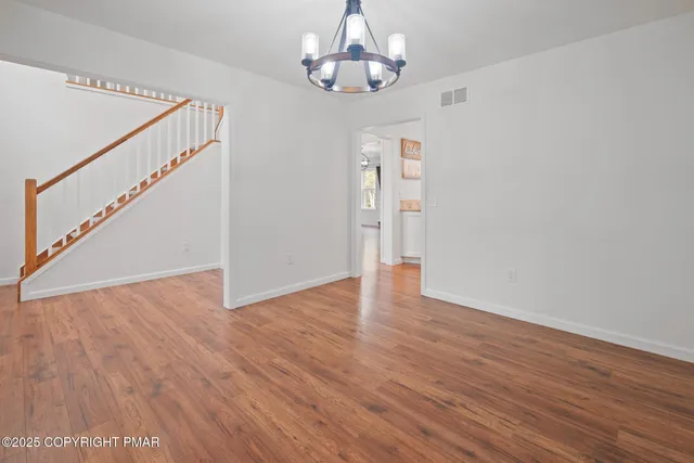 a view of an empty room with wooden floor and a chandelier