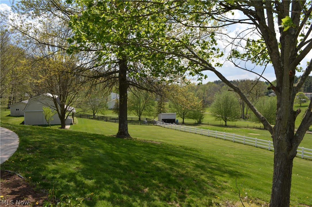 2363 Tabor Ridge Road Northeast New Philadelphia, OH 44663 - Photo 11 of 42 Expansive green lawn featuring a white fence, mature trees, and multiple outbuildings