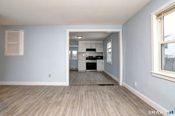 an empty room with wooden floor kitchen view and a window