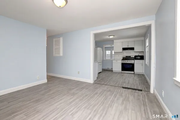 an empty room with wooden floor kitchen view and windows