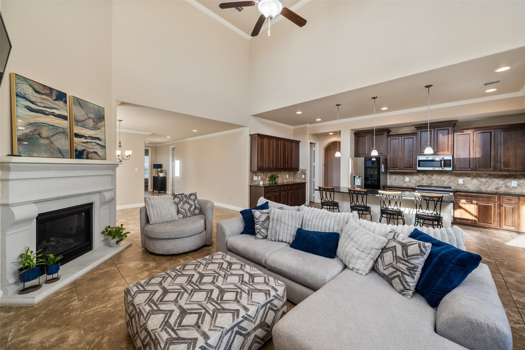 4747 Abercorn Street Rosharon, TX 77583 - Photo 13 of 46 This spacious open-concept living area features high ceilings, a cozy fireplace, and a modern kitchen with dark wood cabinetry and stainless steel appliances. The soft neutral tones and ample natural light create a warm, inviting atmosphere perfect for entertaining.