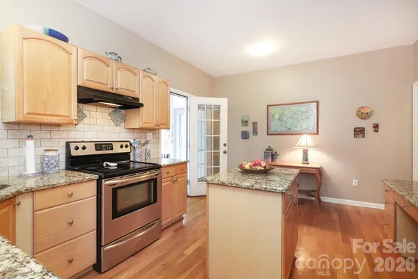 a kitchen with granite countertop a stove a sink dishwasher and white cabinets with wooden floor
