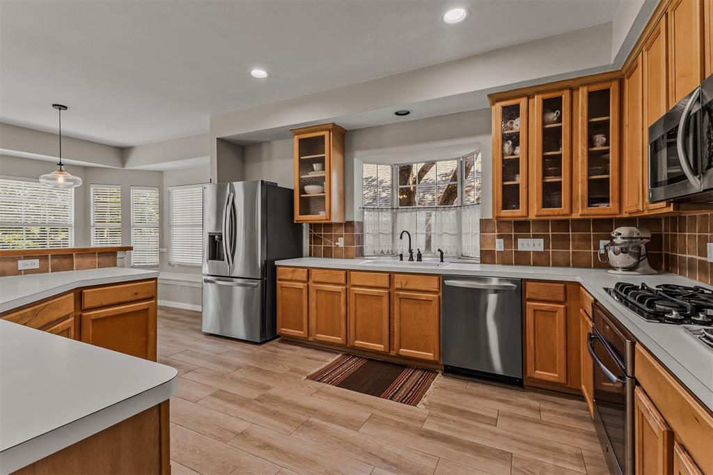 9301 Nottingham Court Rowlett, TX 75088 - Photo 8 of 39 Kitchen featuring wood-finish flooring, light wood cabinetry with some glass-front doors, stainless steel appliances, white countertops, and a tiled backsplash