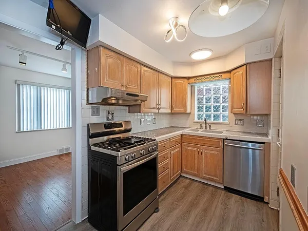 a kitchen with stainless steel appliances granite countertop hardwood floor sink stove and wooden cabinets