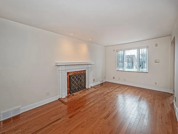 an empty room with wooden floor fireplace and windows