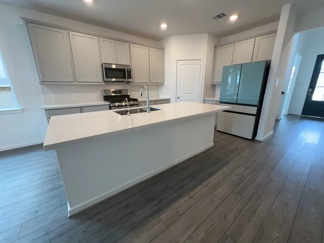 a living room with stainless steel appliances wooden floors wooden cabinets a sink and a stove