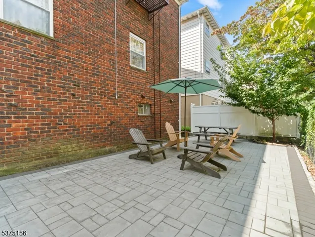 a view of a patio with table and chairs under an umbrella with large trees