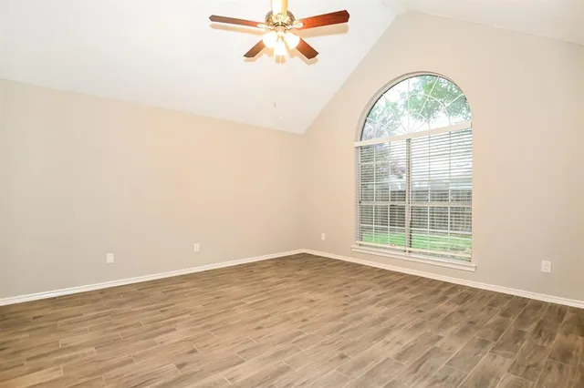 an empty room with wooden floor fan and windows
