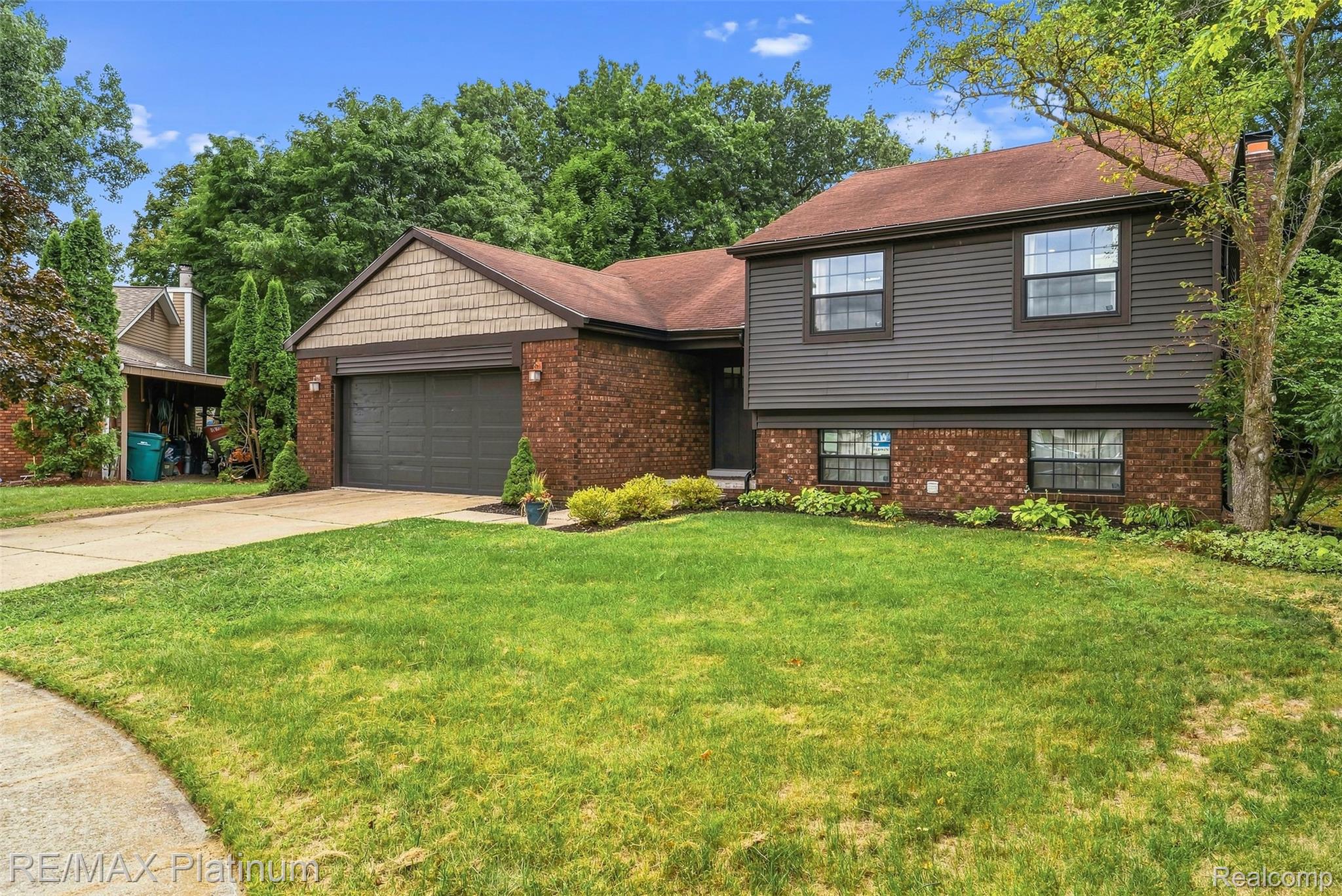 815 Oak Ridge Court Brighton, MI 48116 - Photo 3 of 37 Brick and siding exterior with a dark brown garage door, paved driveway, and established landscaping