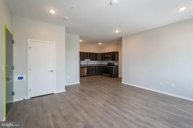 an empty room with wooden floor and kitchen view