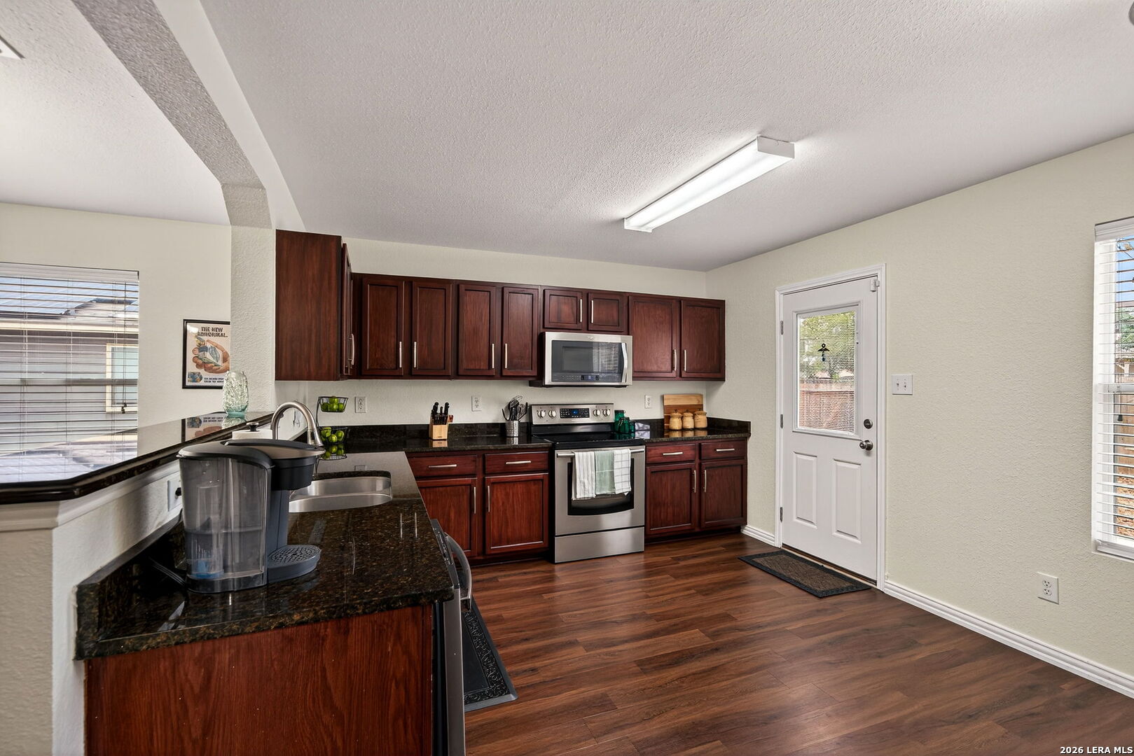 7942 Ruidoso Chase Selma, TX 78154 - Photo 11 of 26 a kitchen with stainless steel appliances granite countertop wooden cabinets a refrigerator a sink a stove a microwave and wooden floors