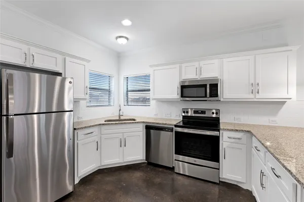 a kitchen with stainless steel appliances granite countertop white cabinets a sink a stove a microwave and a refrigerator