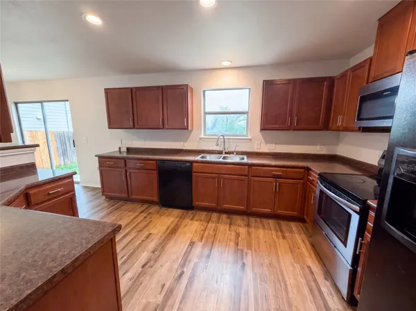 a kitchen with stainless steel appliances granite countertop wooden cabinets a stove top oven a sink and dishwasher with wooden floor