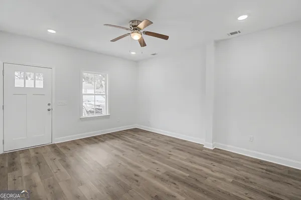an empty room with wooden floor chandelier fan and windows
