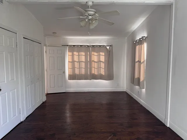 an empty room with wooden floor chandelier fan and windows