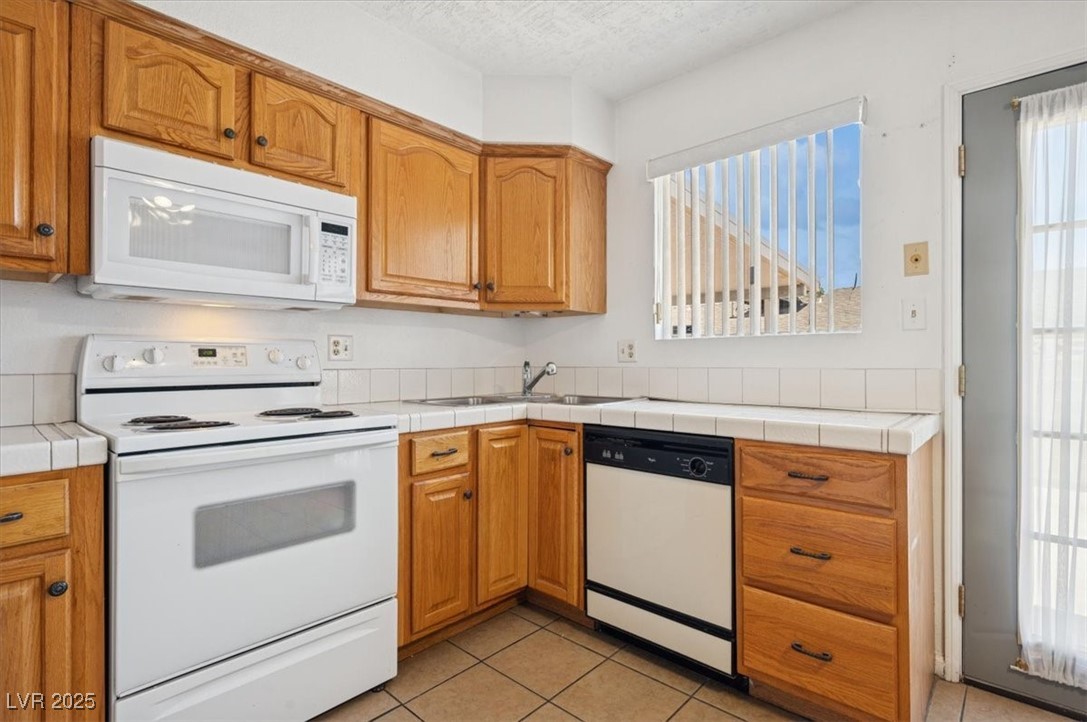 460 Crestway Road Henderson, NV 89015 - Photo 16 of 41 Kitchen featuring white appliances, light tile patterned floors, a sink, brown cabinets, and a textured ceiling
