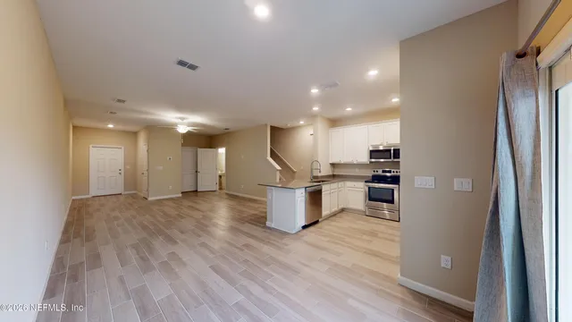 a view of an empty room and kitchen view with wooden floor