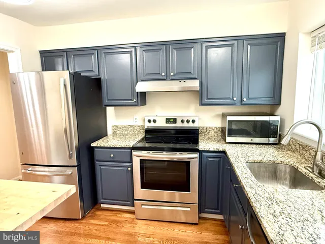 a kitchen with granite countertop a stove a refrigerator and a sink with wooden cabinets