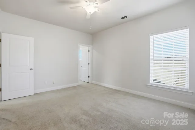 an empty room with chandelier fan and windows
