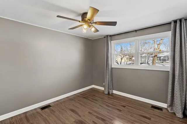 an empty room with wooden floor fan and windows