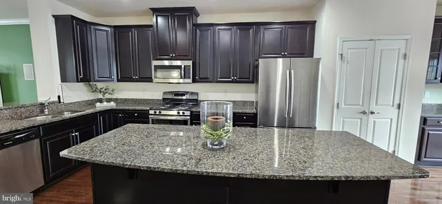 a kitchen with kitchen island granite countertop a sink dishwasher stove and refrigerator with wooden cabinet