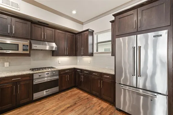 a kitchen with stainless steel appliances granite countertop a refrigerator a sink dishwasher a stove and white cabinets with wooden floor
