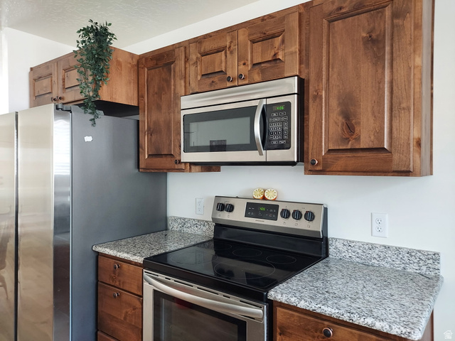 3831 South Powderwood Lane, Unit 111 Mapleton, UT 84664 - Photo 9 of 12 Kitchen featuring wood cabinetry, stainless steel appliances, granite-look countertops, and an electric range with an overhead microwave