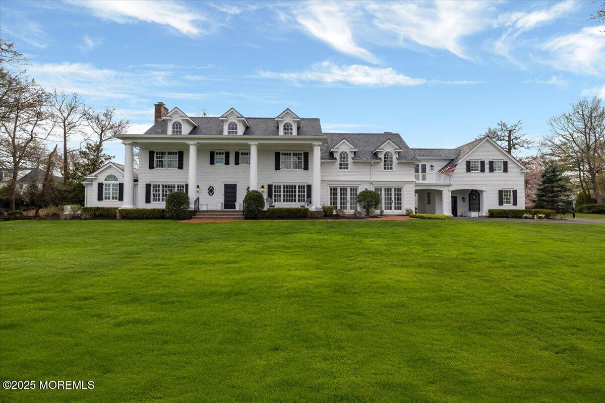a view of a white house with a big yard and potted plants and large tree