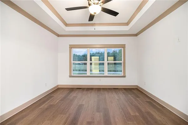 an empty room with wooden floor chandelier fan and windows