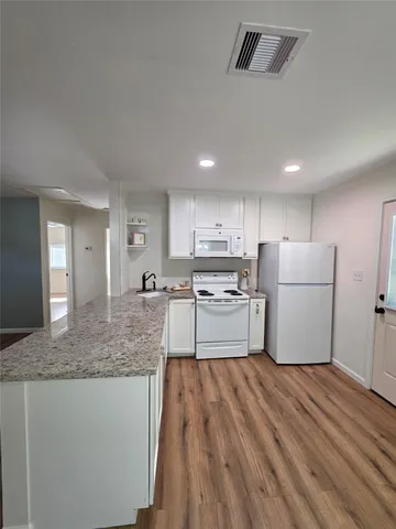 a kitchen with stainless steel appliances granite countertop a sink dishwasher a refrigerator and white cabinets with wooden floor