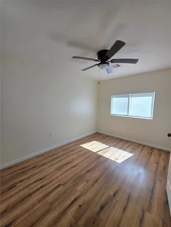an empty room with wooden floor fan and windows
