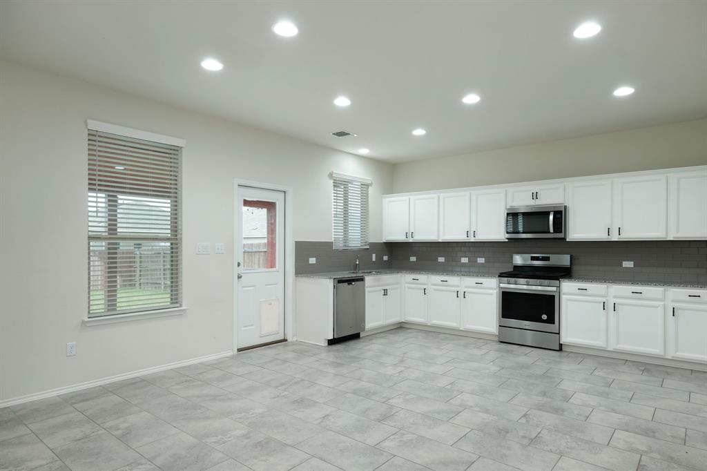 1409 Cliffbrake Way Georgetown, TX 78626 - Photo 2 of 10 Spacious kitchen featuring white cabinetry, stainless steel appliances, a dark speckled countertop, and a gray subway tile backsplash