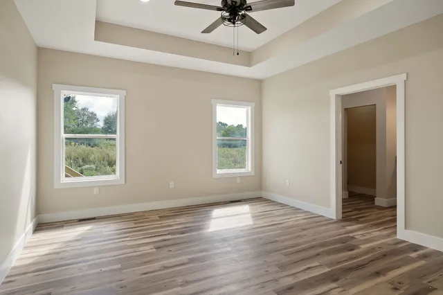 an empty room with wooden floor fan and windows