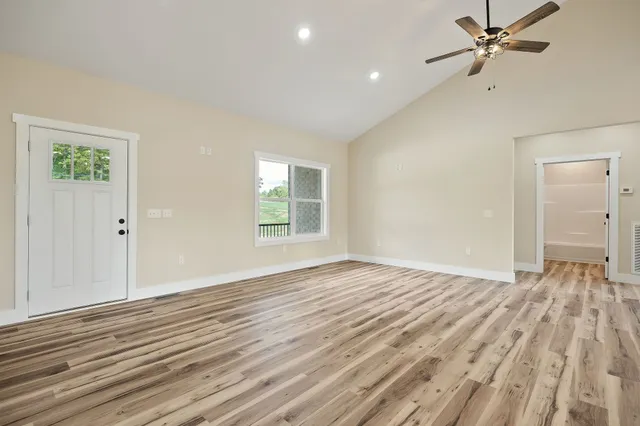 an empty room with wooden floor ceiling fan and windows